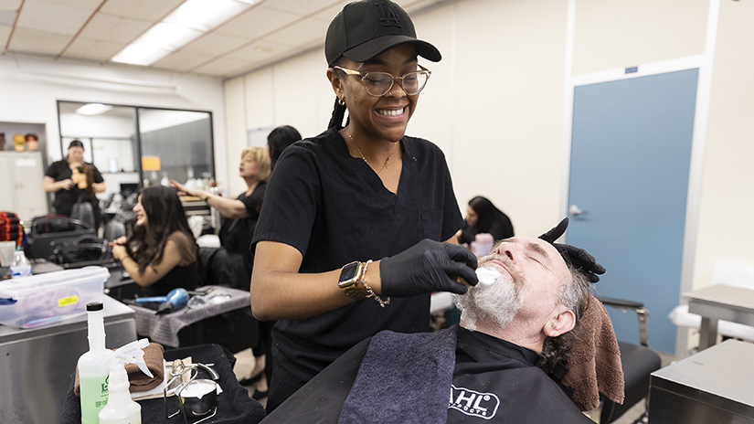 Barbering student Joy providing beard shaving services to client Warren.